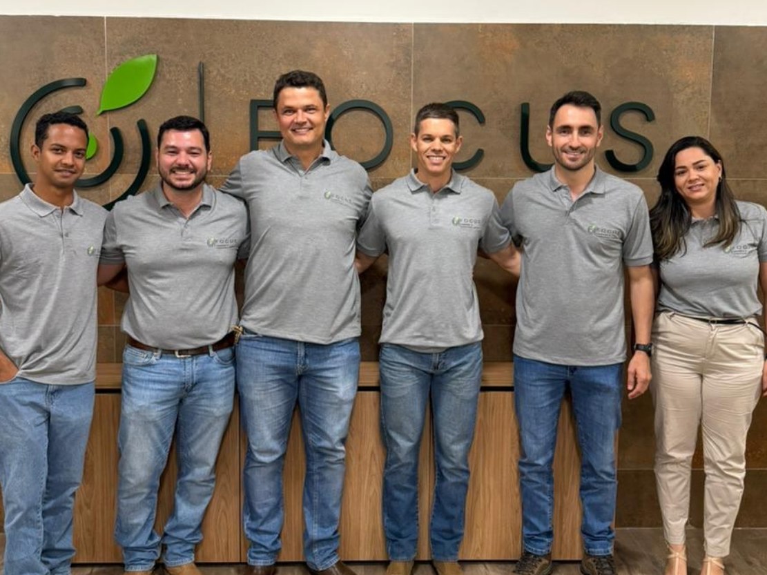 Equipe da FOCUS em frente ao logo, no escritório de Paracatu-MG
